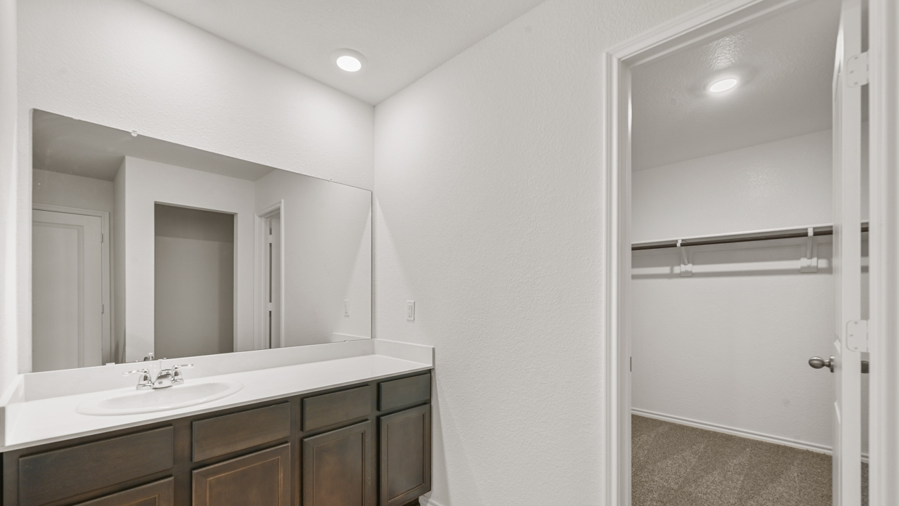primary bathroom with white counters and brown cabinets featuring the spacious closet