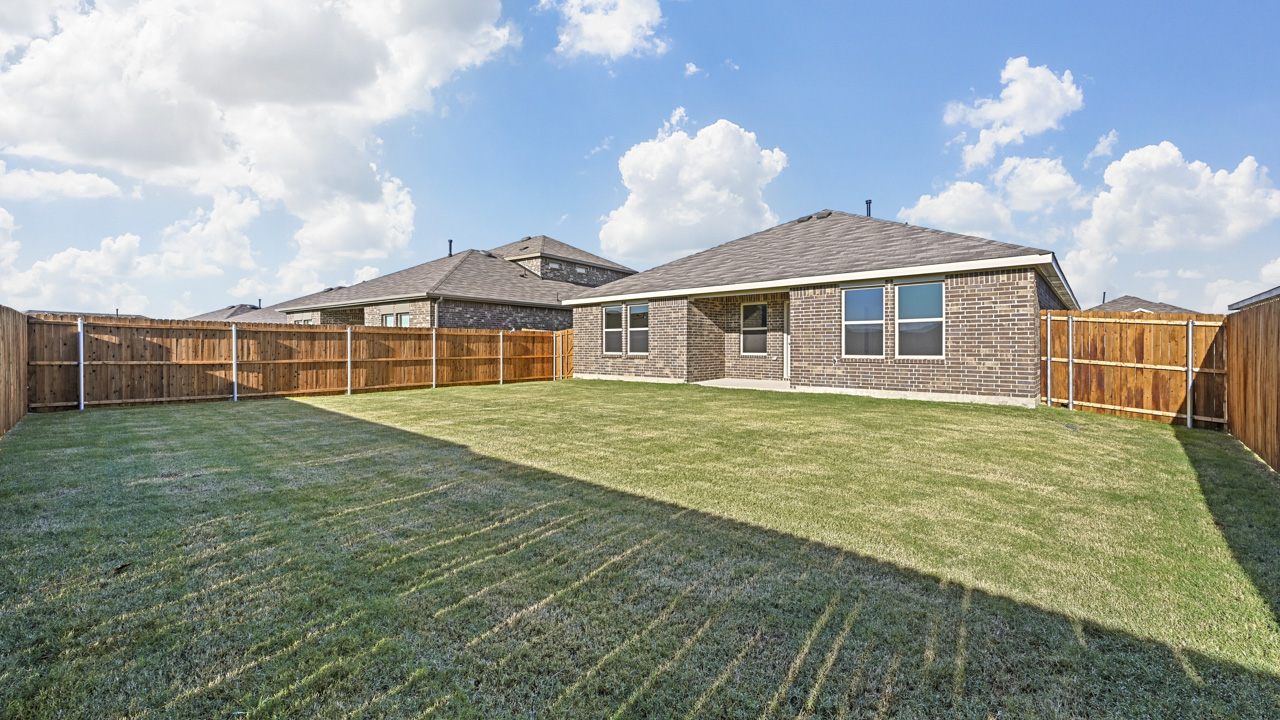 the backyard of a brick home with a covered patio and a wood fence backyard that is covered in grass