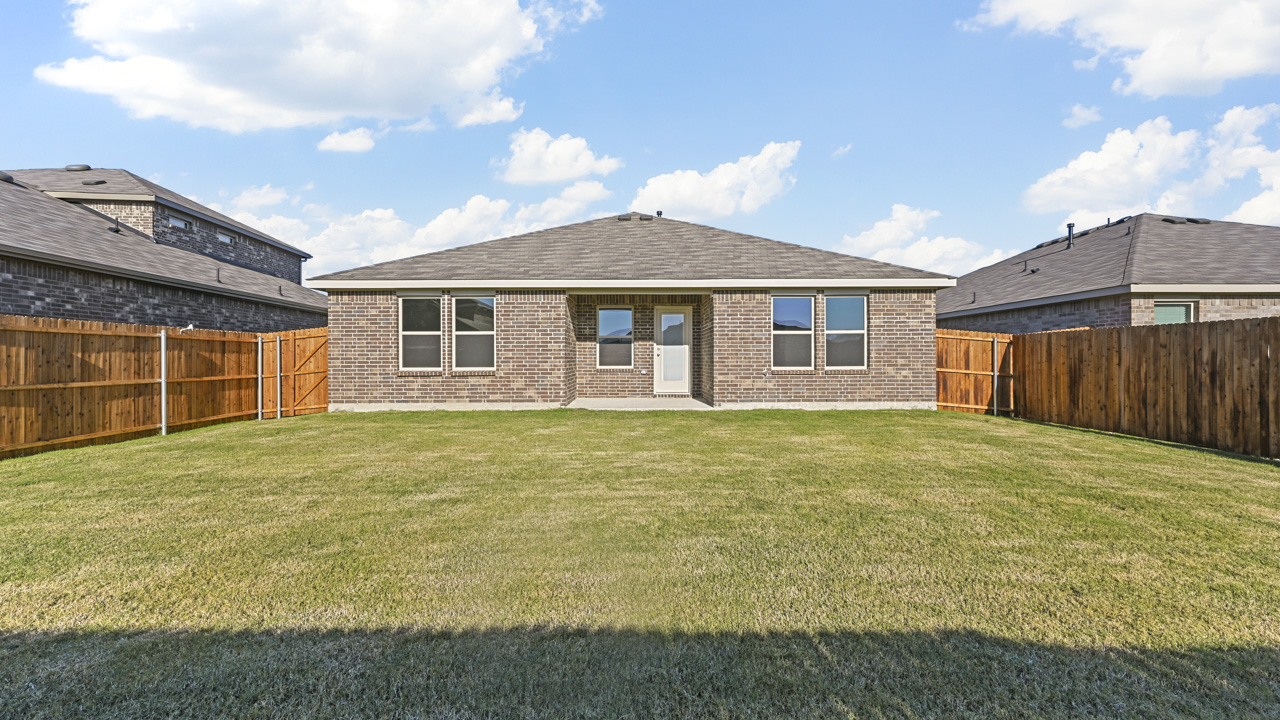 the backyard of a brick home with a covered patio and a wood fence backyard that is covered in grass