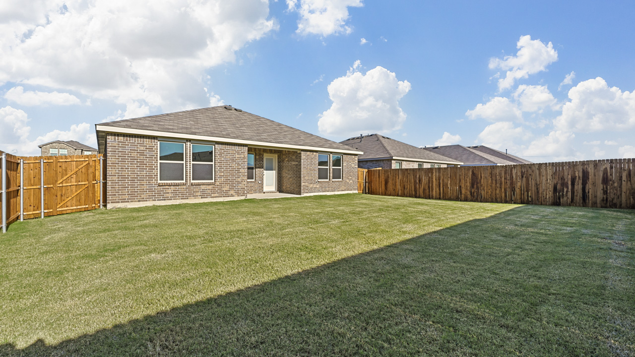 the backyard of a brick home with a covered patio and a wood fence backyard that is covered in grass