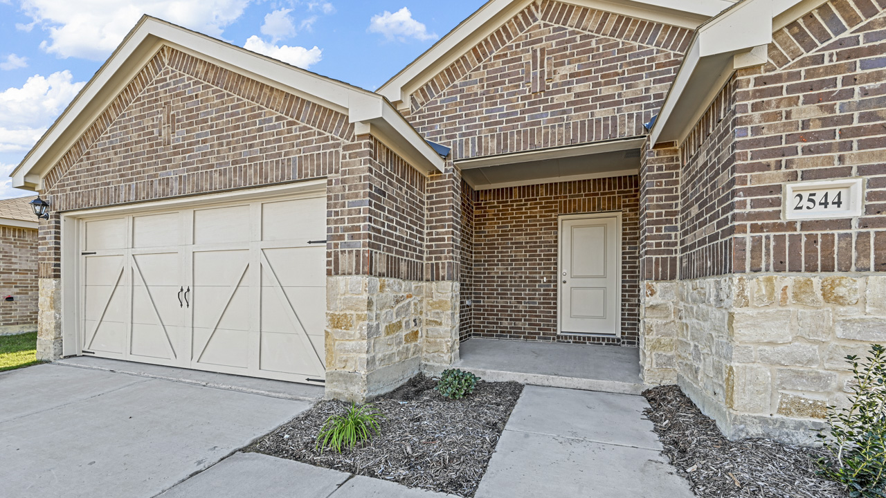 the brick exterior of a one story home with a concrete driveway and a cream colored front door