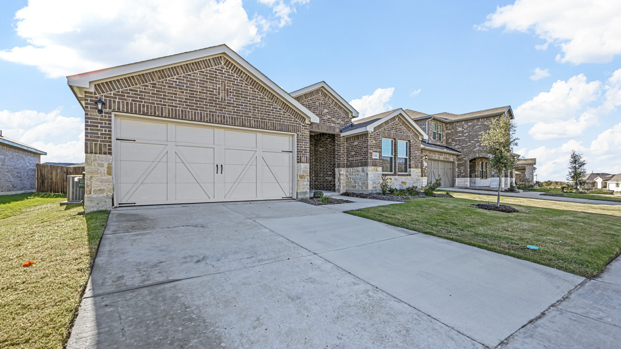 the brick exterior of a one story home with a concrete driveway and a gras covered front yard
