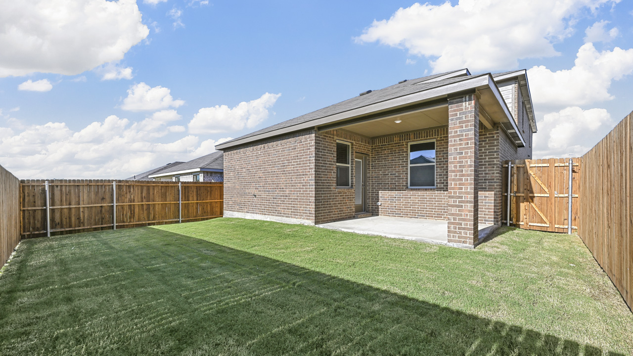 the covered back patio of a brick home with a grass covered yard and a wooden fence