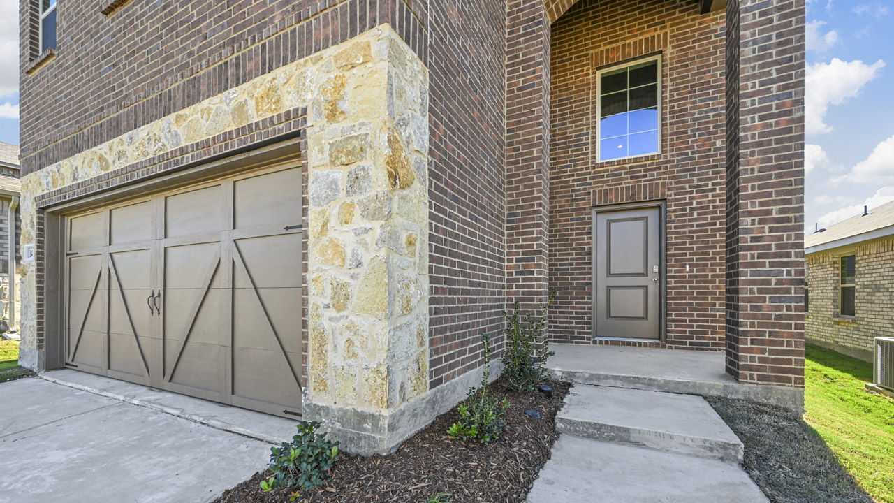 the front door of a brick two story home with a covered patio and concrete sidewalk