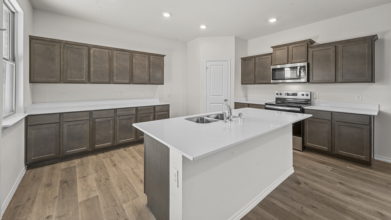 the open kitchen area with dark cabinets wood floors and an island in the middle