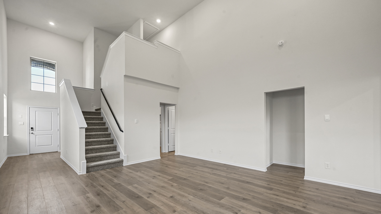 the open living area with white walls and wood floors and the stairwell in the back