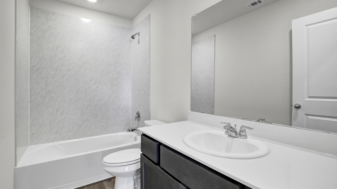 Secondary bathroom with white counters dark cabinets and white bath tub with hardwood floors