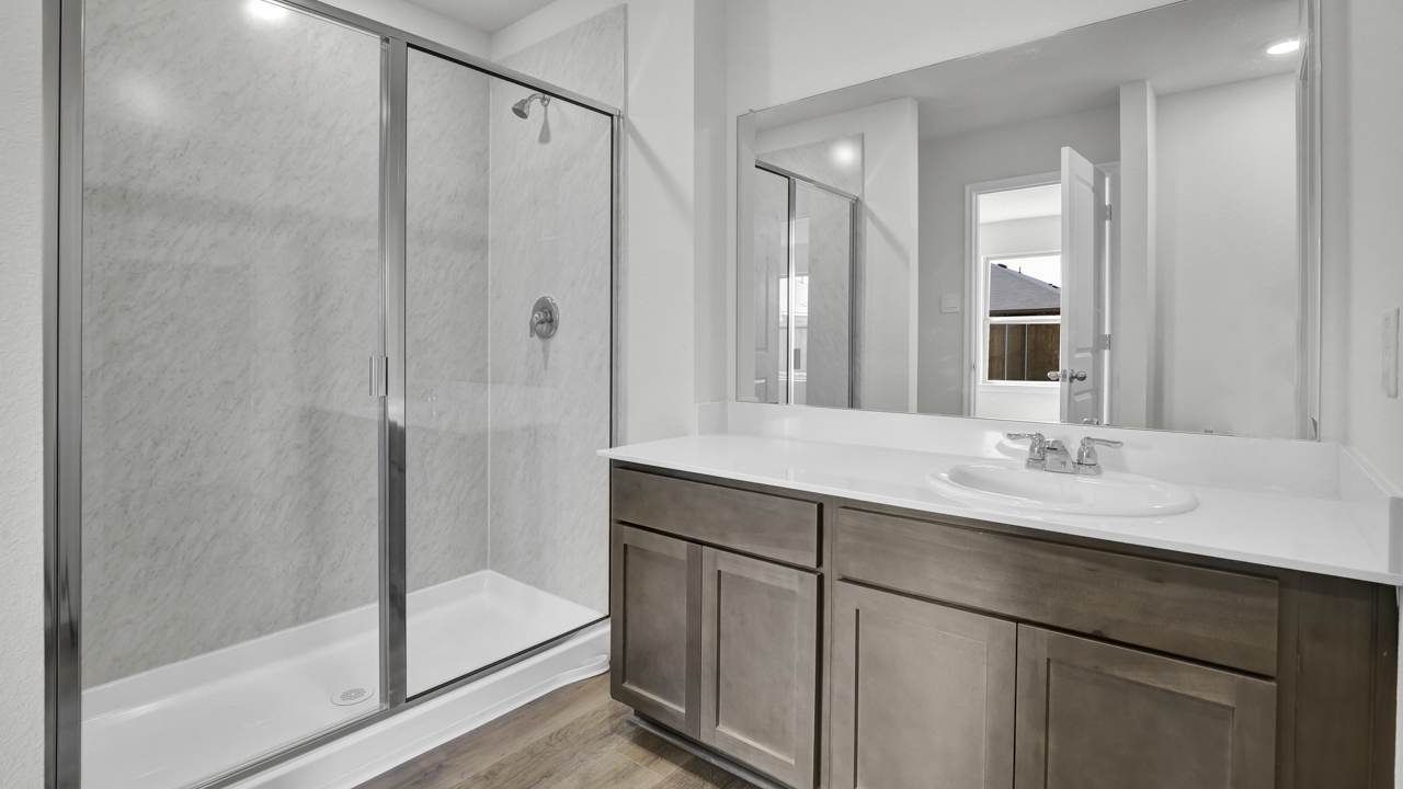 Primary bathroom with glass shower door with light colored counters dark cabinets and hardwood floors