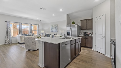 Kitchen island with hard surface countertops, brown cabinets and stainless steel appliances with views into dining area with windows