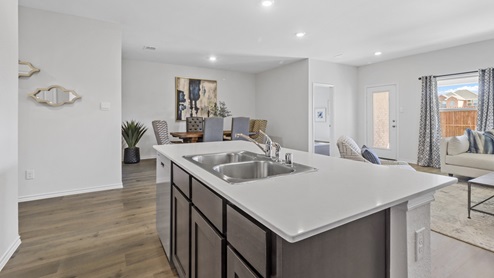 Kitchen island with hard surface countertops, brown cabinets and stainless steel appliances with views into dining area with windows