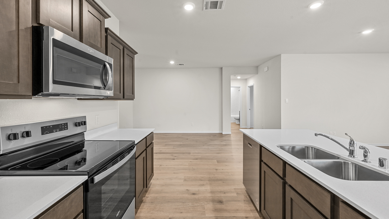 a kitchen with dark cabinets and white walls and wood floors and an island in the middle