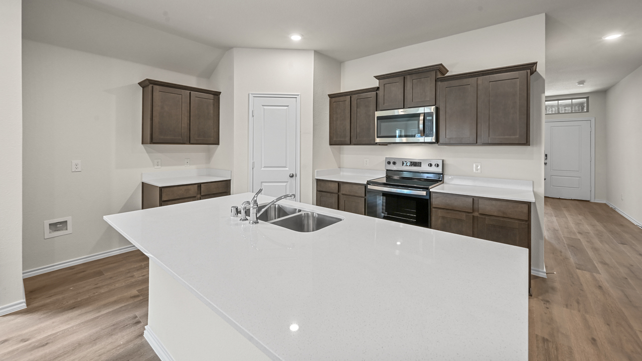 a kitchen with dark cabinets and white walls and wood floors and an island in the middle