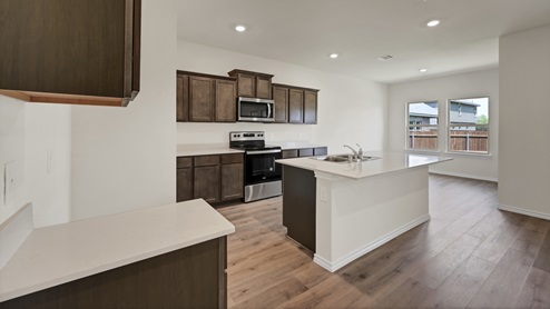 a kitchen with dark cabinets and an island and white walls and wood floors