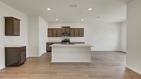 a kitchen with dark cabinets and an island and white walls and wood floors