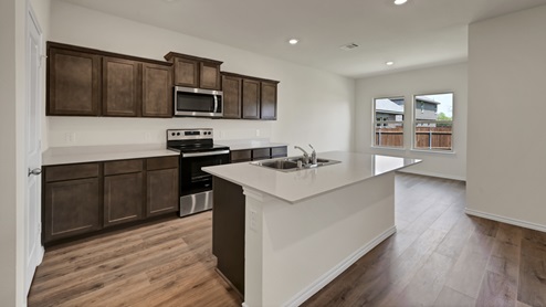 a kitchen with dark cabinets and an island and white walls and wood floors