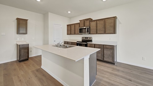 a kitchen with dark cabinets and an island and white walls and wood floors