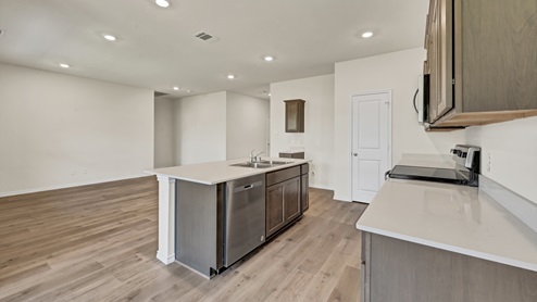 a kitchen with dark cabinets and an island and white walls and wood floors
