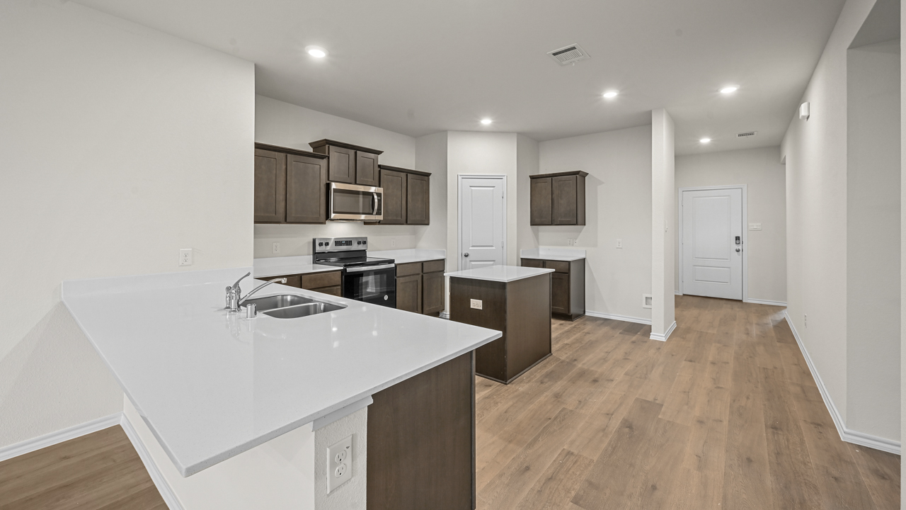 a kitchen with dark cabinets an island in the middle white walls and wood floors