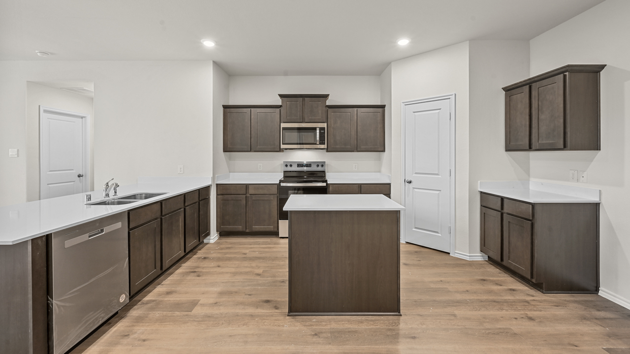 a kitchen with dark cabinets an island in the middle white walls and wood floors