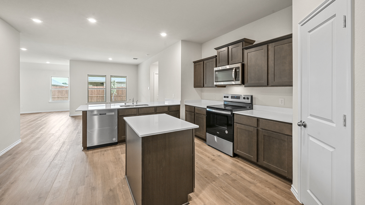a kitchen with dark cabinets an island in the middle white walls and wood floors