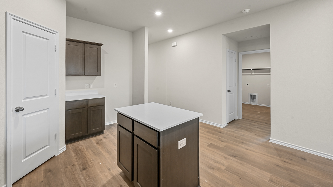 a kitchen with dark cabinets an island in the middle white walls and wood floors