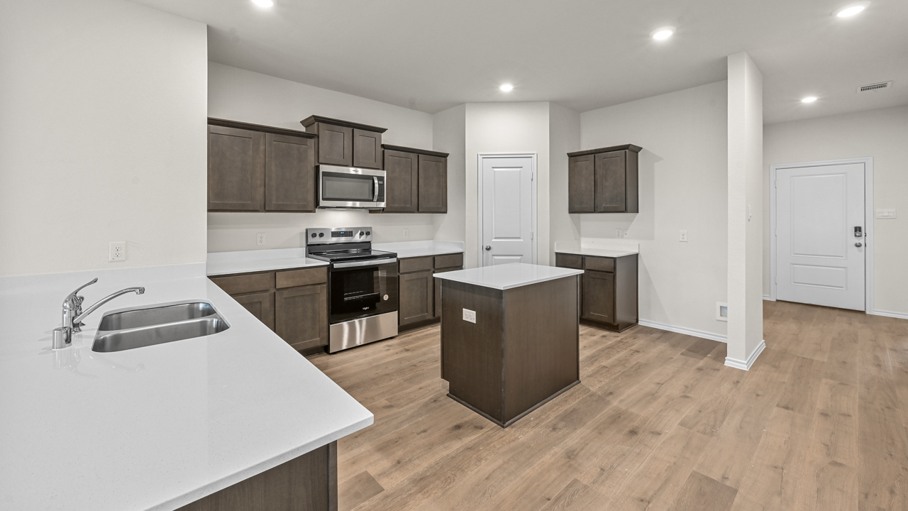 a kitchen with dark cabinets an island in the middle white walls and wood floors