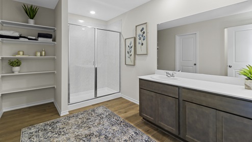 Primary bathroom with white counter vanity and brown cabinets and a stand up shower with shelving to the left