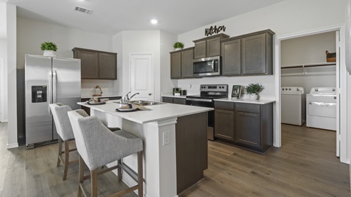 Kitchen island surrounded by white counters, brown cabinets and stainless steel appliances