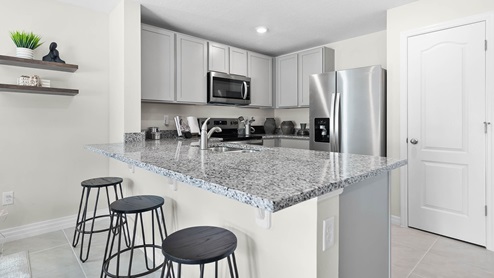 Kitchen with island seating, granite counters, spacious pantry and stainless steel appliances.
