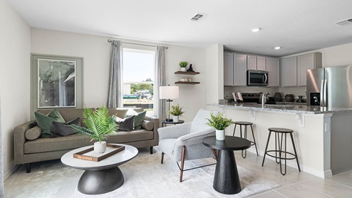 Living area with couch seating and natural lighting adjacent to kitchen counter with granite countertops and stainless steel appliances.