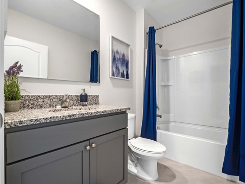Modern bathroom with single bowl sink, granite vanity, wall mirror, cabinets and toilet.