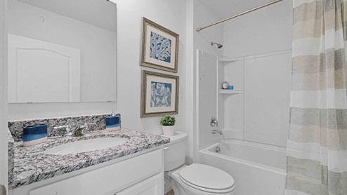 Modern bathroom with single vanity, large wall mirror, cabinets and granite countertops along with walk-in shower