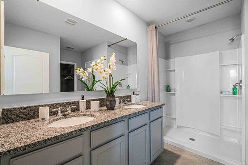 Modern bathroom with double vanity sinks, large wall mirror, cabinets and granite countertops.
