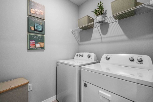 Laundry room with washer and dryer appliances and wall shelving.