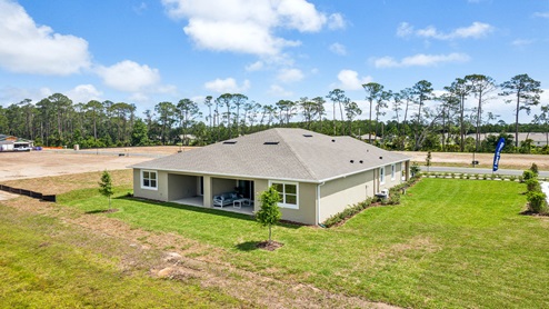 Rear of home with view of grassed backyard, porch seating and slider glass doors.
