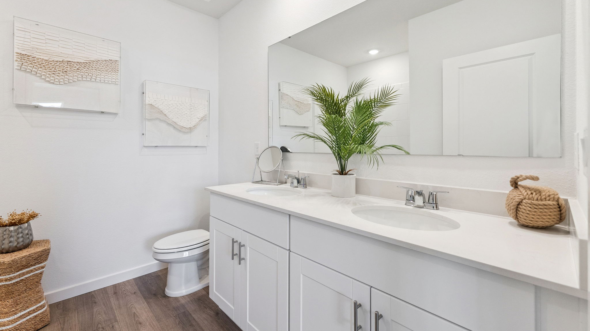 Modern bathroom with double vanity, large wall mirror, cabinets and quartz countertops showing access to master bedroom.