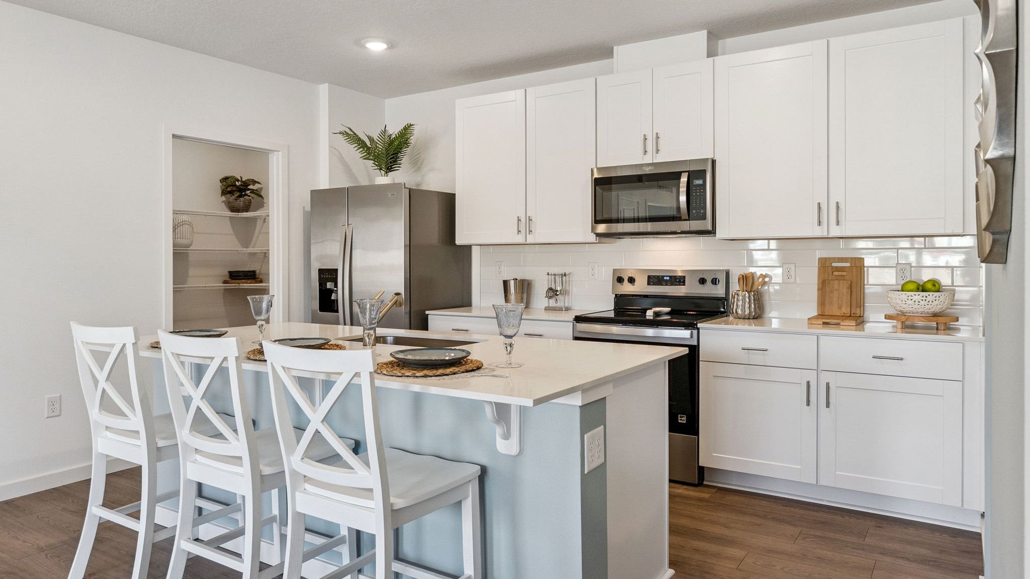 Kitchen with island seating, quartz counters, spacous pantry and stainless steel appliances.