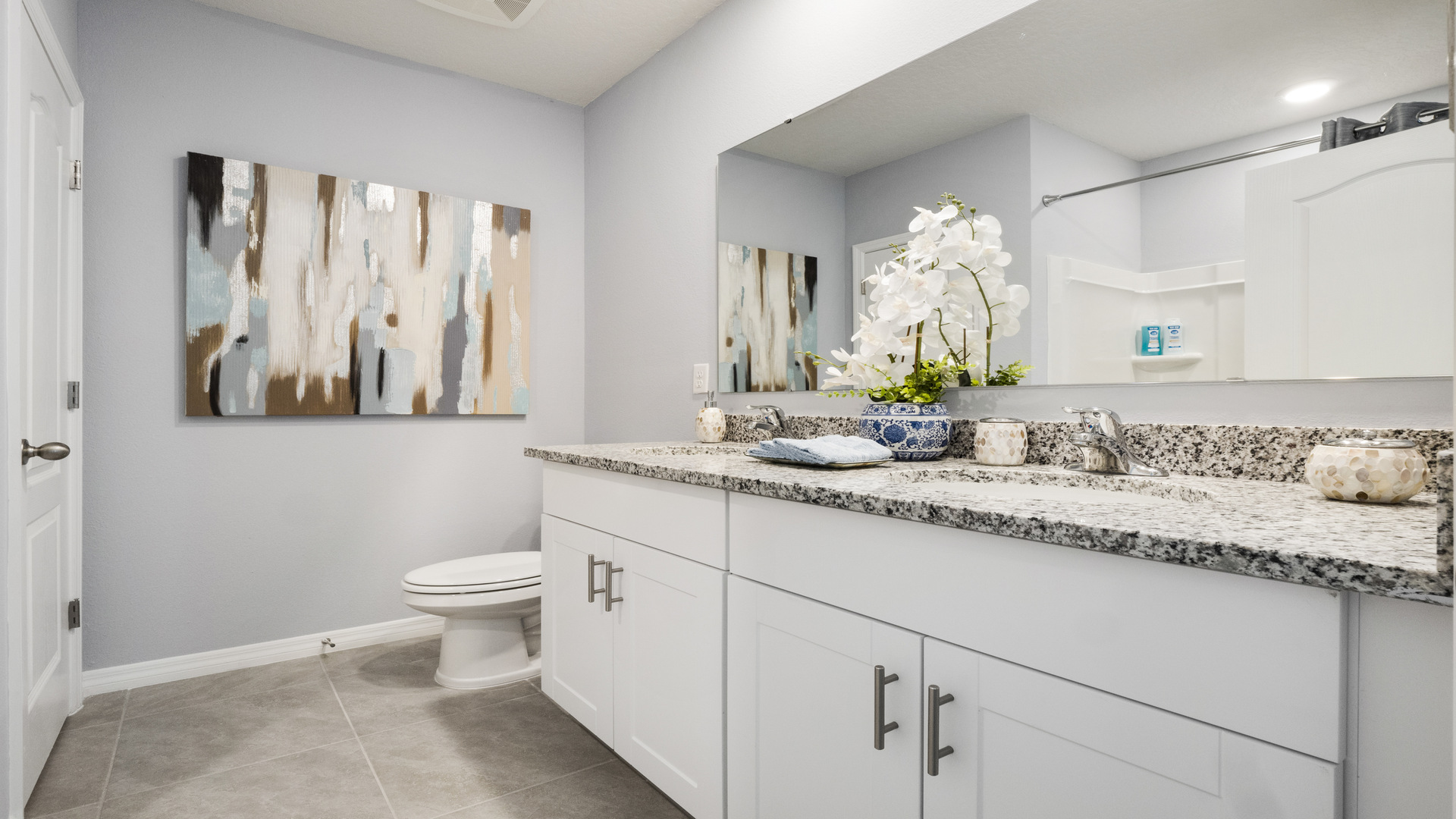Modern bathroom with double vanity sinks, large wall mirror, cabinets and granite countertops.