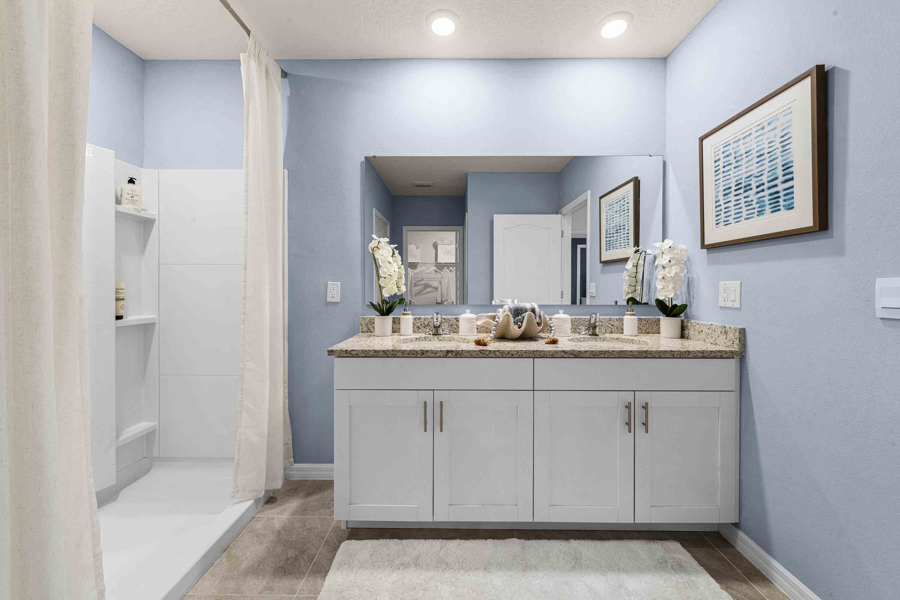 Modern bathroom with double vanity sinks, large wall mirror, cabinets and granite countertops.