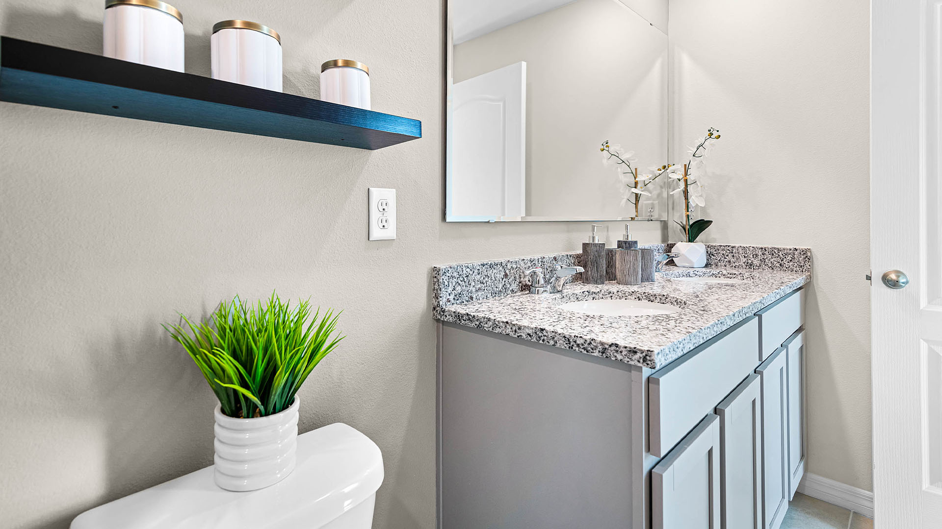 Modern bathroom with single bowl sink, granite vanity, wall mirror, cabinets and toilet.