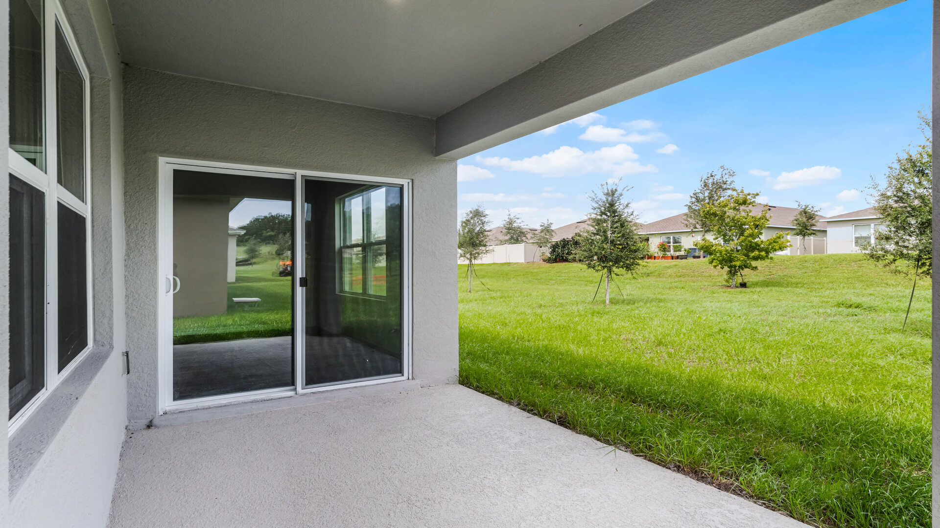 Rear of home with view of grassed backyard, porch seating and slider glass doors.