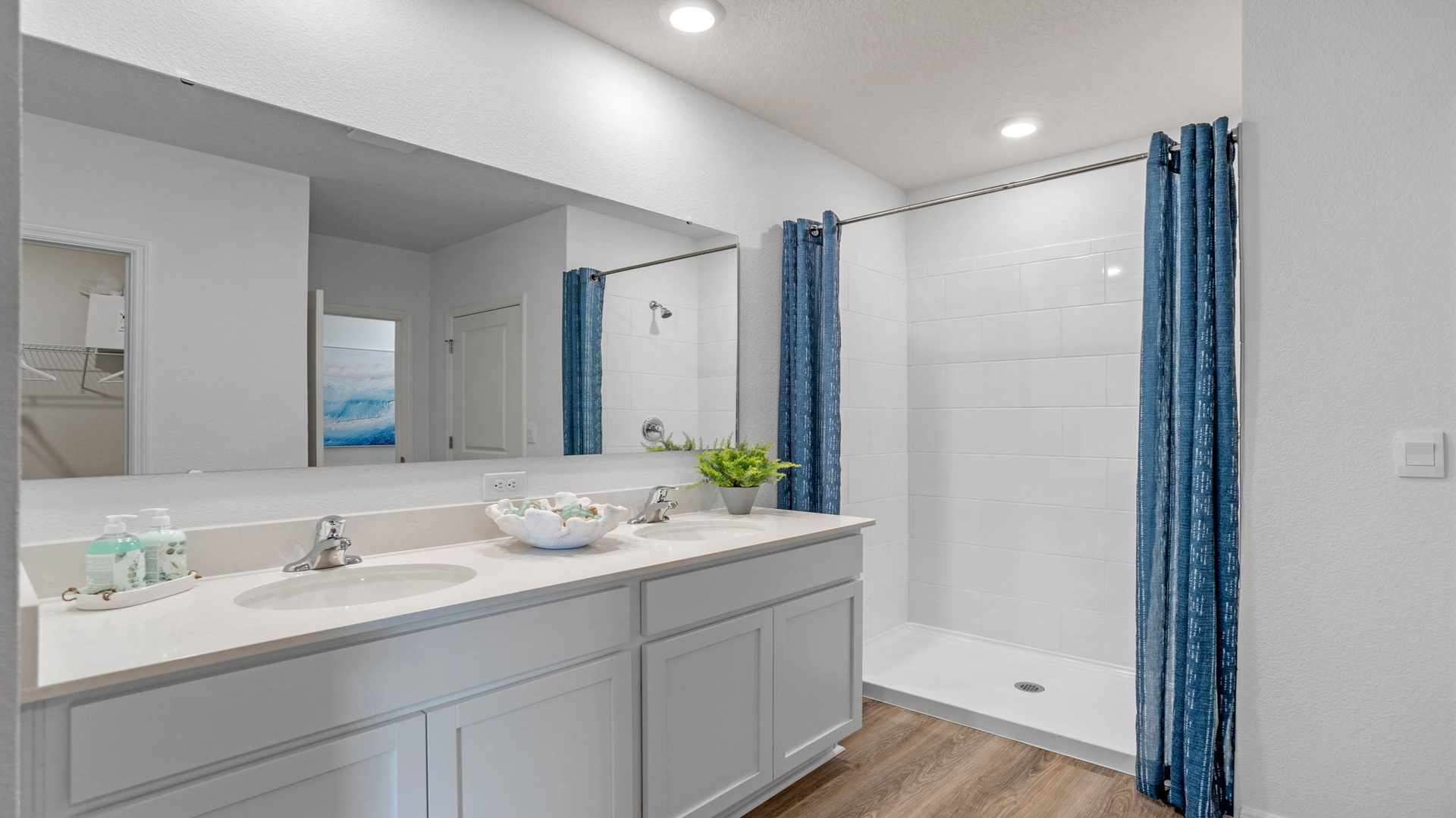 Modern bathroom with double vanity, large wall mirror, cabinets and quartz countertops along with toilet and walk-in shower