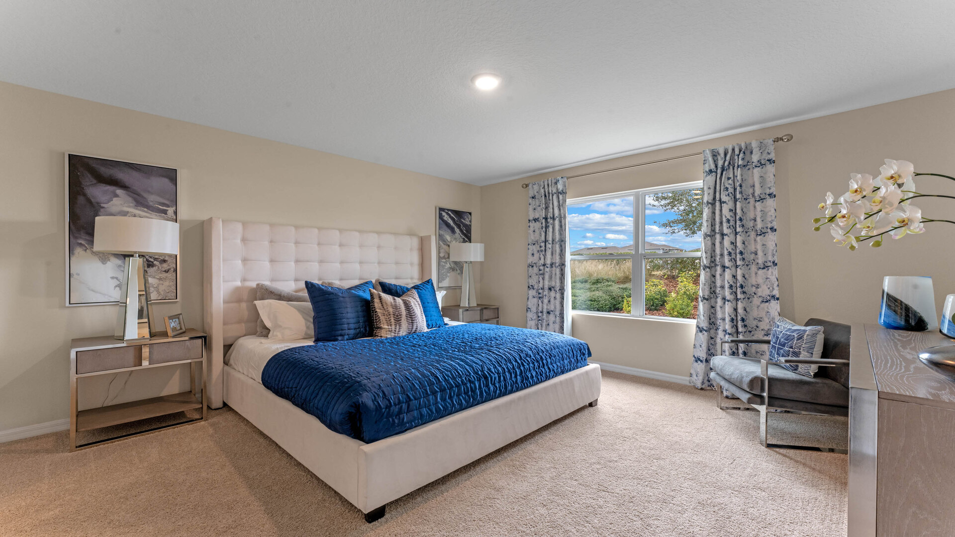 Spacious primary bedroom with king size bed, carpet flooring, natural lighting.