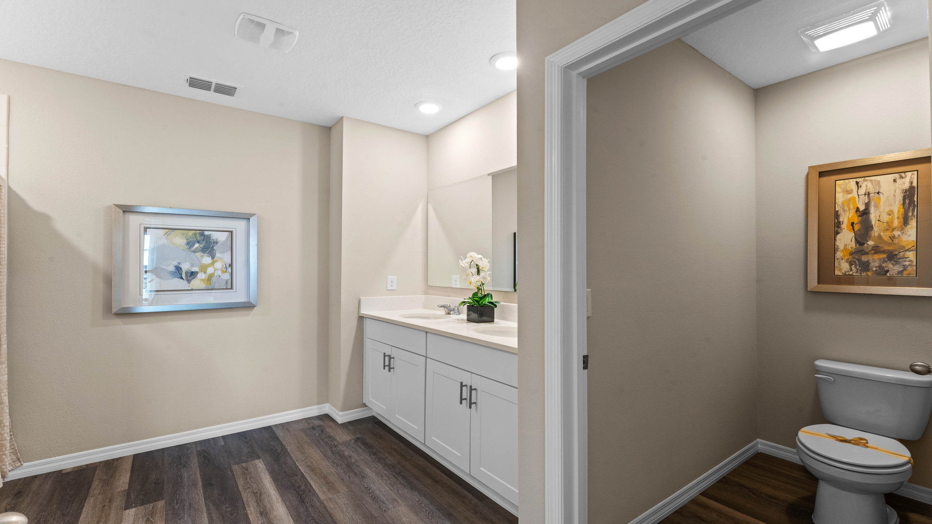 Guest bathroom showing single vanity sinks with quartz countertops, large mirror, and toilet.
