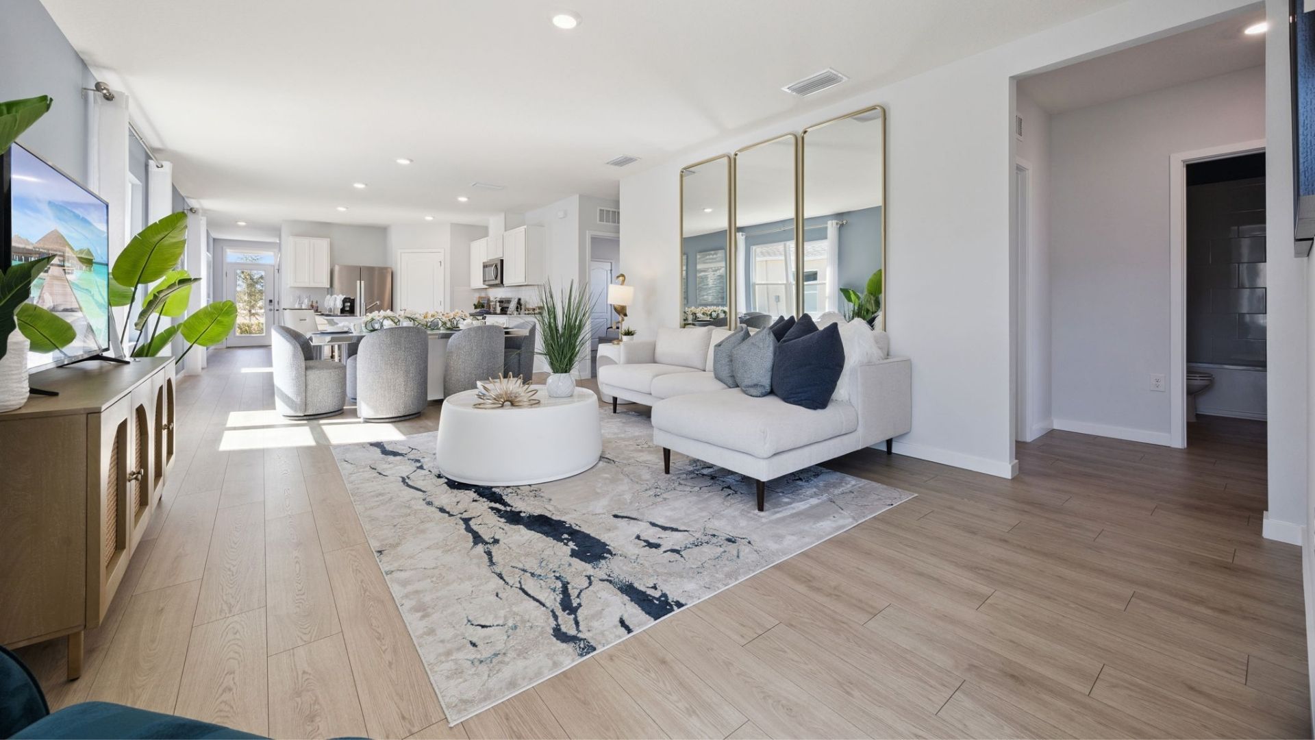 Living area with couch seating, entertainment system and natural lighting overseeing kitchen and dining room