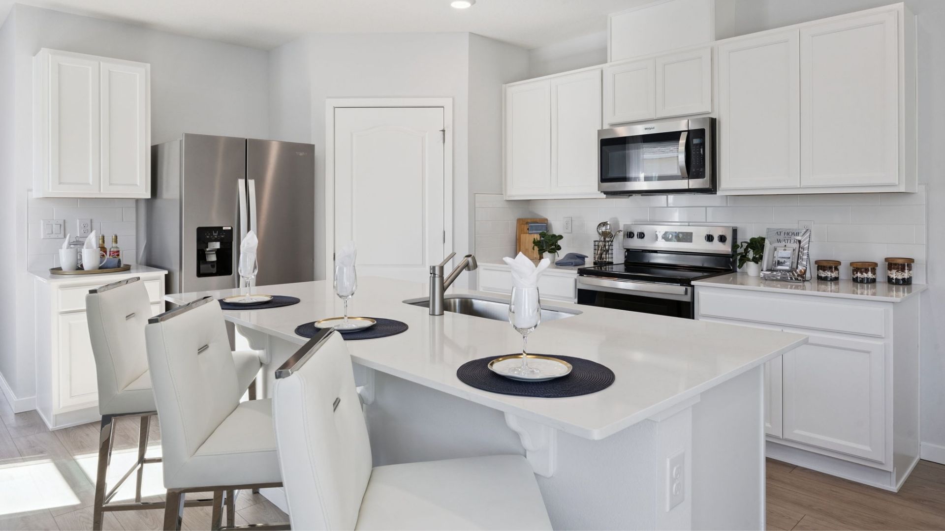 Kitchen with island seating, quartz counters, spacious pantry and stainless steel appliances showing entry way to home overseeing living area.