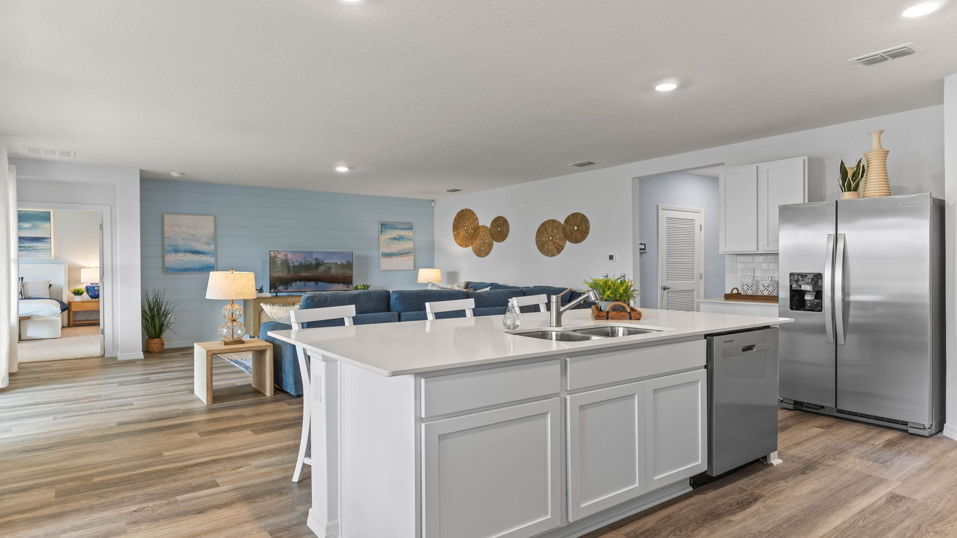 Kitchen with island seating, quartz counters, spacious pantry and stainless steel appliances showing entry way to home overseeing living area.