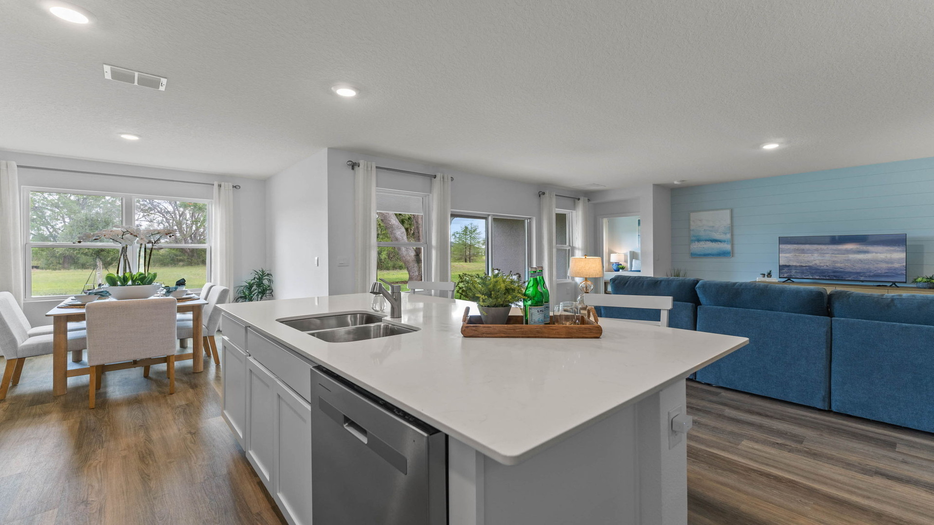 Kitchen with island seating, quartz counters, spacious pantry and stainless steel appliances showing entry way to home overseeing living area.