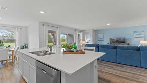 Kitchen with island seating, quartz counters, spacious pantry and stainless steel appliances showing entry way to home overseeing living area.