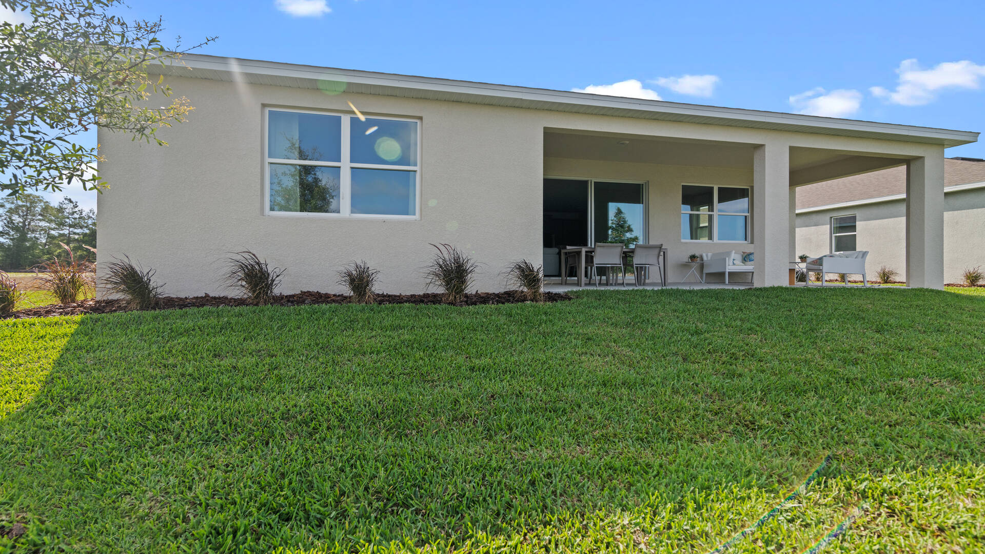Rear of home with view of grassed backyard, porch seating and slider doors.
